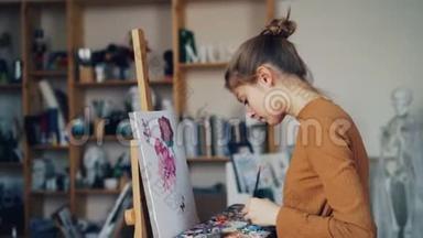 严肃的年轻女士艺术学生正在画室的画布上用画笔和<strong>颜料画</strong>花朵。 生活方式